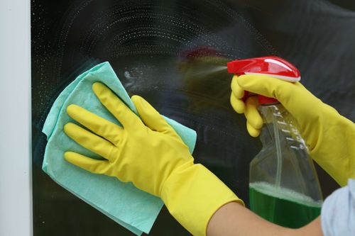 worker spraying cleaning solution on a glass window